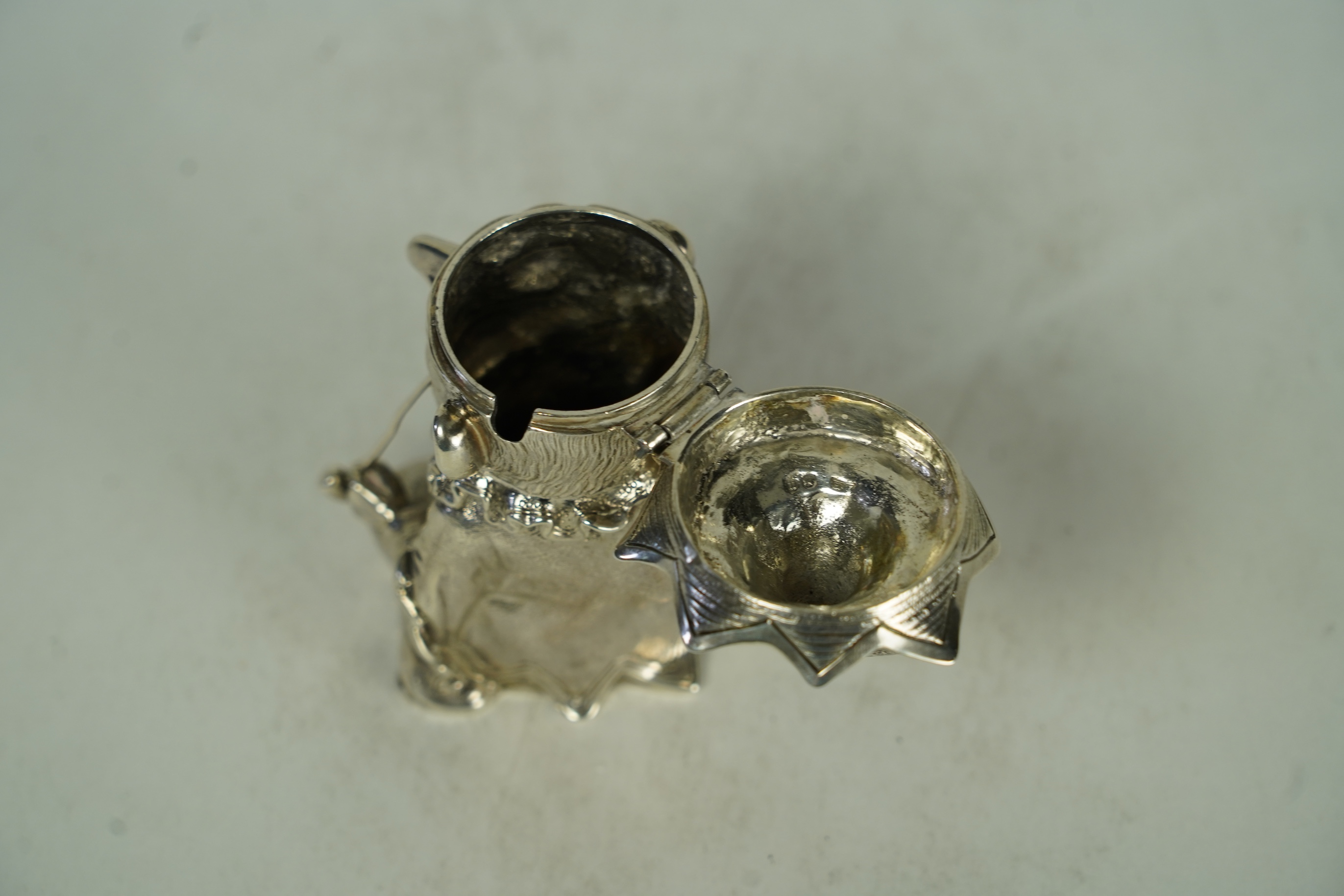 A rare Victorian novelty cast silver mustard pot, modelled as seated cross-legged Mr. Punch, holding a wine glass and smoking a pipe, by Robert Hennell III